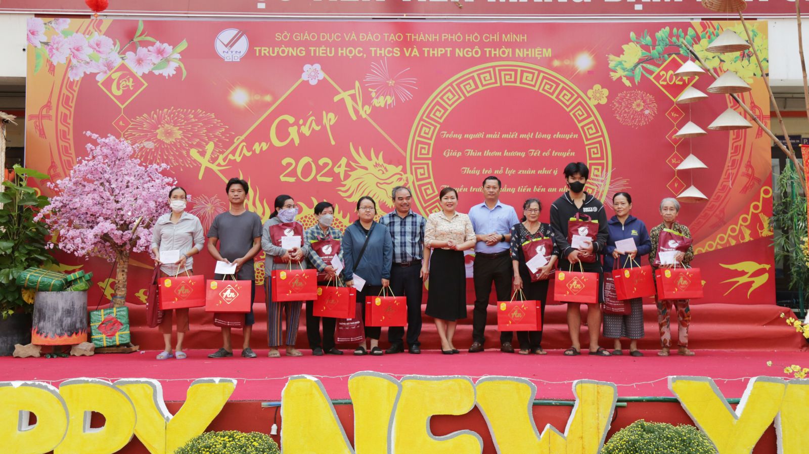 Bà Nguyễn Thị Thanh Xuân - Phó CT UBND Phường Phước Long A (thứ 6 từ trái sang) và thầy Tưởng Nguyên Sự - Hiệu trưởng trường Ngô Thời Nhiệm (thứ 7 từ trái sang) trao quà cho bà con nghèo trên địa bàn phường.